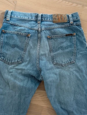 Blå raka jeans från Nudie Jeans W30 L32 - Säljer ett par klassiska blå jeans från Nudie Jeans med raka ben och normal midja. Jeansen har fem fickor, snygga detaljer på bakfickorna och är gjorda i 100% bomull. Perfekta för en avslappnad och stilren look. Modell:steady Eddie II                                          Pris kan diskuteras                                                 Fråga om ni vill ha mått eller mer info.                Storlek: W30 L32