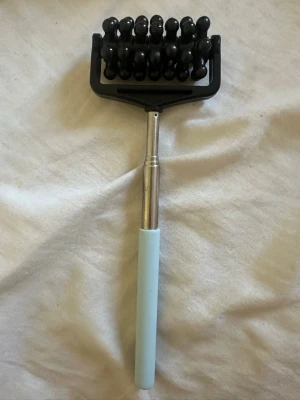 Massageverktyg med blått handtag - Praktiskt massageverktyg med ett ljusblått handtag i plast och ett metallfäste. Huvudet har svarta roterande kulor som ger en skön massage för kroppen. Perfekt för att mjuka upp spända muskler och öka blodcirkulationen.