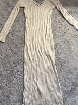 Beige ribbad långklänning BikBok - Långklänning från BikBok i beige ribbat material. Klänningen har lång ärm, v-ringning och en figurnära passform. Perfekt för dig som gillar en enkel men stilren look.