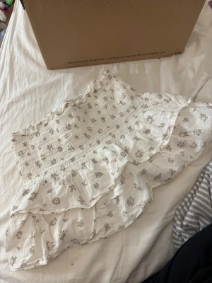 Vit blommig volang kjol - Supersöt vit kjol  med små blommor i rosa och grönt. Kjolen har smock upptill och dubbla volanglager som ger en romantisk känsla. 