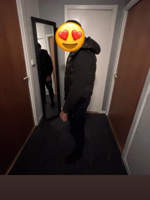Svart dunväst med huva moncler  - Snygg svart moncler väst med glansig finish och huva. Västen har en quiltad design och dragkedja framtill. Perfekt att slänga över en hoodie för en trendig och avslappnad look.