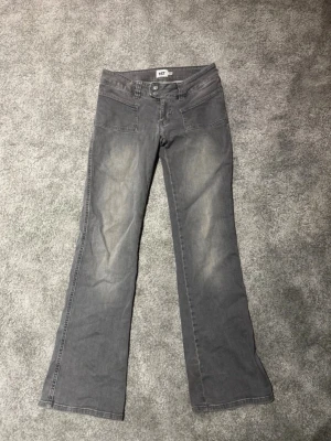 Grå bootcut jeans  - Snygga grå jeans med bootcut passform och diskreta slitningar framtill. Jeansen har klassiska fem fickor och stängs med knapp och dragkedja. Tillverkade i ett mjukt denimtyg som ger en avslappnad look. Finns några skador vid hälen (se bild 3)