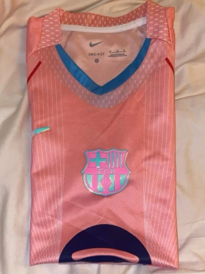 Rosa barcelona tröja - Säljer en rosa FC Barcelona matchtröja från Nike med klubbmärke och Spotify-logga på bröstet. Tröjan har blå detaljer vid kragen och är tillverkad i ett lätt, andningsbart funktionsmaterial. Perfekt för fotbollsträning eller att bära till vardags.