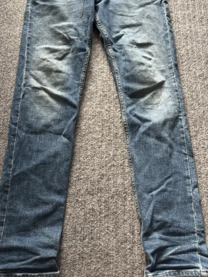 Blå jeans från replay - Säljer ett par klassiska blå jeans från Replay med en snygg passform och snygga slitningar vid knäna. Jeansen har kontrastsömmar och är tillverkade i ett tåligt denimtyg. Perfekta för en avslappnad och trendig look. Dem passar någon som är 170cm ungefär