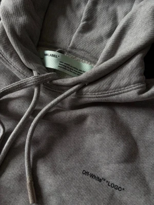 Grå hoodie från Off-White - Snygg grå hoodie från Off-White med trycket. Klassisk passform med huva och dragsko samt en stor magficka framtill. 