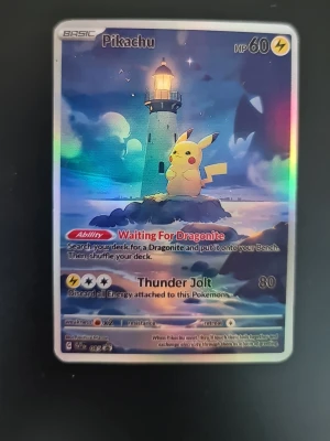 Pokemoncard  Pikachu Nightwatch - Unikt Pokémonkort med Pikachu framför en fyr, holografisk yta som skimrar i regnbågens färger. Kortet har HP 60 och attacker som Thunder Jolt. Perfekt för samlare eller Pokémonfans som vill ha något speciellt i sin samling.