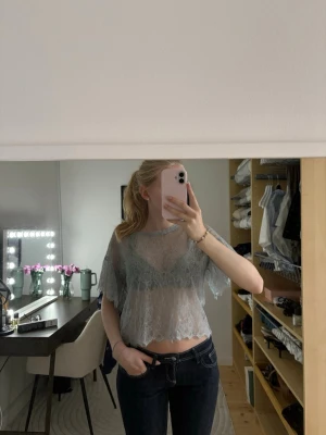 Ljusblå spetsblus med kort ärm - Säljer en ljusblå, transparent spetsblus med korta ärmar och vågig kant nertill. Blusen är croppad och har ett romantiskt uttryck med fina spetsdetaljer. Perfekt att styla över ett linne eller bralette för en trendig look.