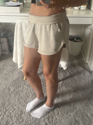 Beige mjuka shorts med resårmidja - Säljer ett par ljusbeige mjuka shorts med bred resår i midjan och rundade benslut. Shortsen har en relaxed passform och är perfekta för varma dagar eller chill hemma. Tillverkade i ett skönt bomullsmaterial. Lite slitna men rätt söta.