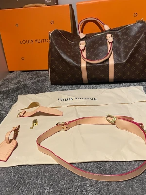 Louis Vuitton Monogram Keepall 50 - Säljer en klassisk Louis Vuitton Keepall 50 i brunt monogram canvas med ljusa läderdetaljer och guldiga metalldelar. Väskan har både handtag och avtagbar axelrem, perfekt för resor. Kommer med hänglås, nyckel och bagageta samt dustbag.