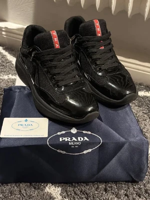 P Skor - Säljer ett par svarta P sneakers med glansiga detaljer och meshpaneler. Skorna har snörning, rund tå och tydlig röd P-logga på plös och häl. Snygg och modern design i skinn och textil, perfekta för dig som gillar unika skor. i storlek 42. rabatt, kan erbjudas vid snabb affär.
