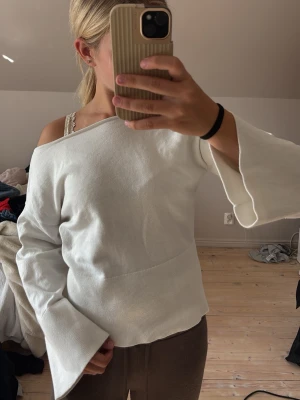 Vit offshoulder topp med vida ärmar - Säljer en vit offshoulder topp med vida, långa ärmar och ribbad struktur. Toppen har en avslappnad passform och är perfekt för dig som gillar en trendig och stilren look. Materialet känns mjukt och bekvämt mot huden.