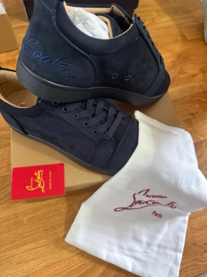 Mörkblåa sneakers från Christian Louboutin - Snygga mörkblåa sneakers i mocka från Christian Louboutin med ton-i-ton snörning och diskret broderad logga på sidan. Skorna har en klassisk låg silhuett och svart sula. Kommer med originalpåse och kort.