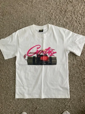 Cortiez no time 4 luv Vit t-shirt med grafiskt tryck - Säljer en vit t-shirt i bomull med ett stort grafiskt tryck framtill som föreställer en digital klocka och rosa graffiti. Klassisk passform och rund hals. Perfekt för dig som gillar streetwear och unika prints.