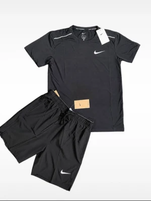 Nike Miller set - Snyggt svart träningsset från Nike med Dri-Fit teknologi. Setet består av en t-shirt och shorts, båda med vita Nike-loggor. Perfekt för löpning eller gym. Materialet är lätt och andas, vilket gör det bekvämt under intensiva pass.
