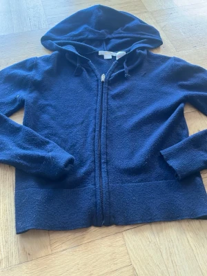 Mörkblå hoodie från Gina Tricot - Mysig mörkblå hoodie från Gina Tricot med dragkedja framtill och huva. Tillverkad i mjukt material och har ribbade muddar vid ärmslut och nederkant. Perfekt för en avslappnad stil.