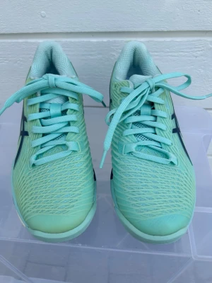 Oanvända Asics SolutionFF 2 stl 37,5 - Säljer ett par mintgröna Asics träningsskor med mesh-ovandel och mörkblå detaljer på sidorna. Skorna har snörning och en sportig, lätt design som passar perfekt till gymmet eller löprundan. Sulan är vit med inslag av blått och grått för extra stil. Helt nya, endast provade. Nypris 1600 kr