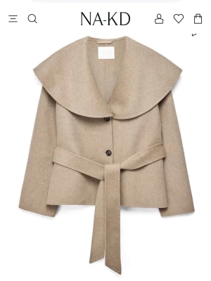 Beige kappa med stor krage från NA-KD - Trendig beige kappa från NA-KD med oversized krage och knytskärp i midjan. Kappan har två knappar framtill och raka ärmar. Tillverkad i ett mjukt material som ger en stilren och modern look.