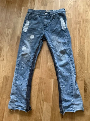 Blå jeans gallery depth - Säljer ett par blå jeans med slitna detaljer och vita pärlor längs benen. Jeansen har raka ben, råa kanter nertill och är gjorda i 100% bomull. Perfekta för dig som vill ha en unik och trendig look.