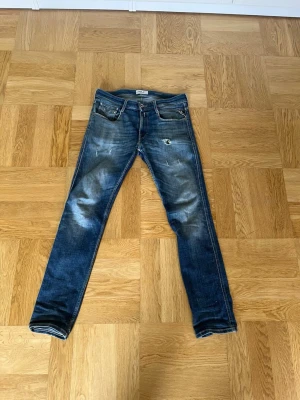 Mörk Blå slingor replay jeans med slitningar - Säljer ett par mörkblå slim jeans med slitningar och tvättade detaljer. Jeansen har fem fickor, knappgylf och kontrastsömmar. Passformen är smal och benen är raka. Perfekta för en avslappnad och trendig look. Ny pris 1899