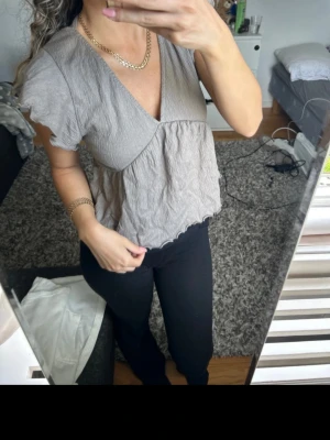 Beige volangblus med v-ringning - Säljer en luftig beige blus med v-ringning och volangdetaljer vid ärmslut och nederkant. Blusen har korta ärmar och en avslappnad passform som ger en skön och trendig look. Perfekt att styla med jeans eller kjol för en chill vibe.