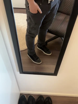 Grå slitna jeans med hål - Säljer ett par grå jeans med skinny fit och flera slitningar och hål på benen för en trendig, avslappnad look. Jeansen har klassisk femficksmodell och är tillverkade i denim. Perfekta för dig som gillar streetstyle och vill ha en edgy vibe.