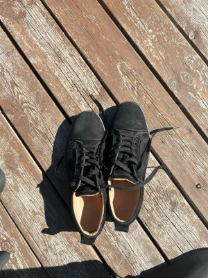Svarta låga sneakers med röd sula - Snygga svarta sneakers med lågt skaft och klassisk snörning. Ovandelen är i tyg och sulan är svart med en cool röd undersida och grafiskt mönster. Passar perfekt till streetwear och vardagsstil.
