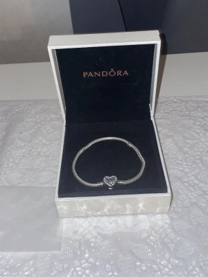 Pandora silverarmband  - Säljer ett stilrent silverfärgat armband från Pandora. Armbandet har en ormkedja och en hjärtformad berlock med infinity-symbol och små gnistrande stenar. Perfekt för dig som gillar klassiska smycken med en twist.