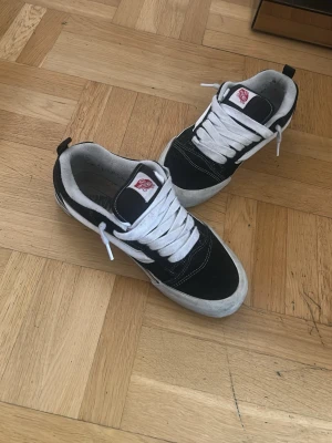 Svarta och vita Vans Old Skool sneakers - Klassiska Vans Old Skool sneakers i svart och vitt med vit sula och vita skosnören. Skorna har den ikoniska sidoremsan och är tillverkade i mocka och canvas. Perfekta för en avslappnad streetstil.