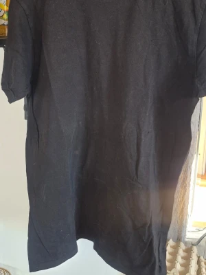Svart basic t-shirt - En enkel svart t-shirt i klassisk modell med rund hals och korta ärmar. Perfekt att matcha med jeans eller shorts för en clean look. Tillverkad i mjukt bomullstyg som känns skönt mot huden.