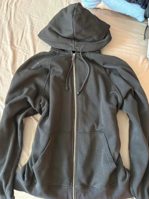 Svart zip hoodie med huva - En klassisk svart hoodie med dragkedja framtill och stor huva. Hoodien har två rymliga fickor på magen och justerbara snören i huvan. Tillverkad i mjukt och bekvämt material, perfekt för chill dagar eller när du vill ha en enkel och stilren look.