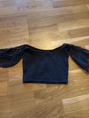 Mörkblå croppad topp med spetsärmar - Trendig mörkblå croppad topp med vida, genombrutna spetsärmar. Toppen har en fyrkantig ringning och är tillverkad i ett stickat material som ger en snygg struktur. Perfekt för dig som vill ha något unikt och stilrent.