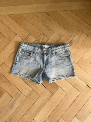 Ljusblå jeansshorts med broderade fickor - Säljer ett par ljusblå jeansshorts med fina detaljer och fransiga kanter. Shortsen har broderade bakfickor och klassisk femficksdesign. Perfekta för sommardagar och har en avslappnad, trendig look.