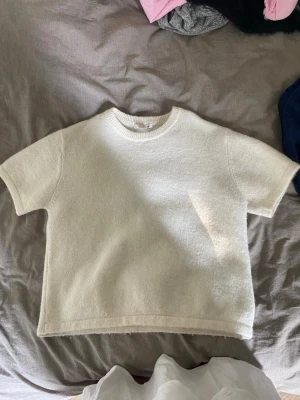 Vit kortärmad stickad topp - En enkel och stilren vit stickad topp med korta ärmar och rund hals. Toppen har en mjuk struktur och rak passform, perfekt att matcha med jeans eller kjol för en clean look. Passar till allt.
