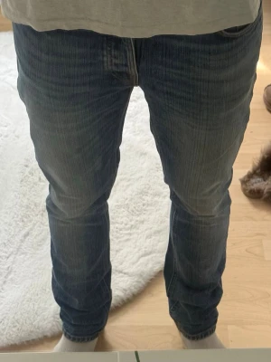 Blå raka jeans med slitningar - Säljer ett par klassiska blå jeans med raka ben och snygga slitningar. Jeansen har fem fickor, normal midja och kontrastsömmar. Perfekta för en avslappnad och trendig look. Materialet är denim i bomull. Modellen är grim Tim. Storlek 30/32