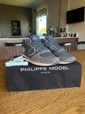 Philippe Model grå TRPX - Snygga sneakers från Philippe Model i mörkgrå mocka och textil med vita detaljer. Klassisk låg modell med vita sulor och matchande grå skosnören. Skorna har en ikonisk sköldlogga på sidan och kommer med extra skosnören. Kan gå med på prisförslag 
