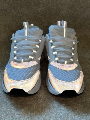 Dior b22 sneakers med reflexdetaljer - Säljer ett par grå chunky sneakers med mesh- och syntetmaterial, samt reflekterande detaljer på ovansidan och hälen. Skorna har vita och ljusrosa inslag och tjock sula för extra streetkänsla. Perfekta för dig som gillar sportig och modern stil.