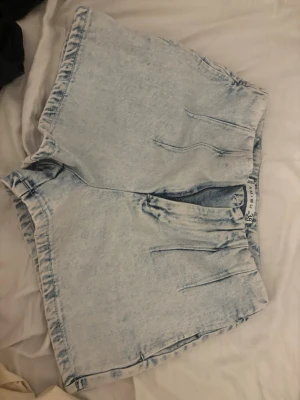 Ljusblå denimshorts från Amisu - Säljer ett par ljusblå denimshorts från Amisu i storlek 38. Shortsen har hög midja, avslappnad passform och klassisk femficksdesign. Perfekta till sommaren och lätta att matcha med olika toppar.