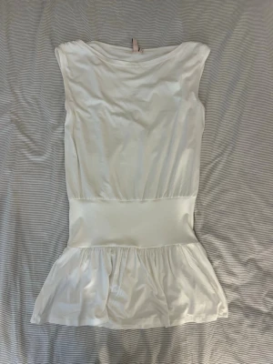 Vit kort klänning från Nelly - Säljer en vit kort klänning från Nelly. Klänningen har en markerad midja och volang nedtill som ger en feminin siluett. Perfekt för dig som vill ha en enkel men snygg look.