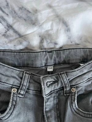 Grå bootcut jeans från Kappahl - Säljer ett par gråa bootcut jeans med klassiska fem fickor. Jeansen har bälteshällor och stängs med knapp och dragkedja. Perfekta för dig som gillar en avslappnad men ändå trendig look.