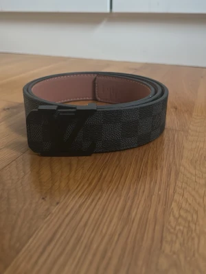 Svart-rutigt bälte i skinn - Snyggt svart bälte med klassiskt rutigt mönster. Bältet är gjort i skinn och har en stilren design som passar till många olika outfits. Pris kan diskuteras 