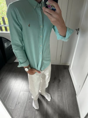 Grön Oxford Ralph Lauren skjorta - Klassisk och stilren skjorta från Polo Ralph Lauren som passar både till vardags och lite mer uppklädda outfits. Jag är 180 cm / 70 kg och bär storlek S på bilderna.  Skjortan är i mycket fint skick utan defekter. Inga fläckar, hål eller andra skador.  Modell: Polo Ralph Lauren Oxford Shirt Storlek: S Nypris: ca 1 550 kr Skick: Mycket fint skick  Mått:  * Längd: 70 cm * Bredd: 45 cm * Ärmlängd: 61 cm  📦 Postas inom 24 timmar! 📸 Se bilder för skick och passform.