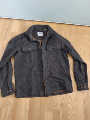 Brun overshirt från Jack & Jones - Snygg brun overshirt från Jack & Jones i storlek XS. Skjortjackan har två bröstfickor med knappar, klassisk krage och knäppning framtill. Perfekt nu till hösten eller våren. Nästan intill ny, används ca 2-3 gånger. Passar dig som är ca 165-170. Riktigt snygg till svarta kläder. Pris kan diskuteras!