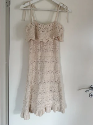 Beige stickad klänning från Zara - Supersöt beige stickad klänning från Zara med smala axelband och volang upptill. Klänningen har ett fint hålmönster och vågig kant längst ner. Perfekt för sommarens alla tillfällen!