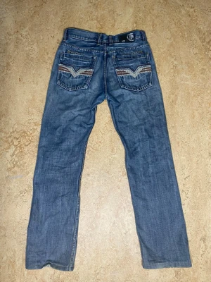 MISSA INTE UT! Diesel jeans 🪄  - Säljer ett par blå jeans med raka ben och snygga broderade detaljer på bakfickorna. Jeansen har klassisk femficksdesign och en patch med tryck i midjan. Perfekta för en avslappnad och trendig stil.