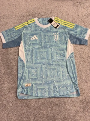 Juventus matchtröja blå Adidas - Snygg Juventus matchtröja i ljusblått med vitt och gula detaljer. Tröjan har ett unikt mönster, klubbmärke och Adidas-logga på bröstet samt nummer 10 och namnet Yildiz på ryggen. Tillverkad i lätt och ventilerande funktionsmaterial.