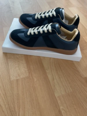 Svarta sneakers med beige detaljer - Snygga sneakers i svart med beige insida och vita snören. Skorna har en klassisk låg siluett med gummisula i brunt och ovandel i en mix av mocka och slätt material. Perfekta för en stilren och avslappnad look.storlek 41. Skriv om ni har frågor!