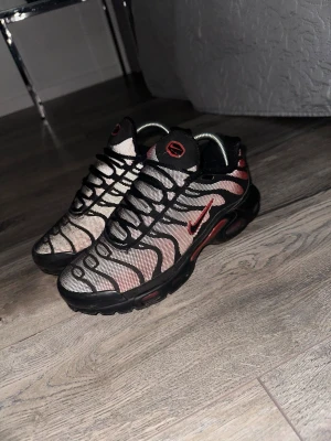 Svarta och röda sneakers med mesh - Säljer ett par snygga sneakers med svart och röd färgkombination. Skorna har ett mesh-överdrag med vågiga svarta linjer och röda detaljer, inklusive en röd logga på sidan. Sulan är svart och designen är sportig och modern.