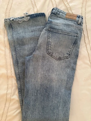 Ljusblå mom jeans från Gina Tricot - Säljer ett par ljusblå mom jeans från Gina Tricot med hög midja och raka ben. Jeansen har en snygg sliten detalj vid benslutet och klassisk femficksdesign. Perfekta till en avslappnad och trendig look.