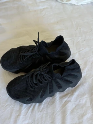 Svarta sneakers med vågig sula - Säljer ett par helsvarta sneakers med unik vågig sula och mesh-överdel. Skorna har snörning och en sockliknande passform som ger en modern och sportig look. Perfekta för dig som vill sticka ut med din stil.