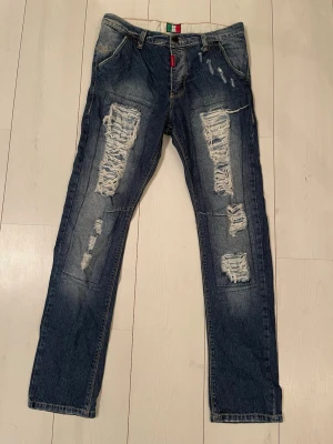 Adrian Hammond Jeans - Säljer ett par blå jeans med kraftiga slitningar och hål på framsidan. Jeansen har raka ben, klassisk femficksmodell och detaljer i form av slitna partier. Materialet är denim och de har en cool, avslappnad vibe. 
